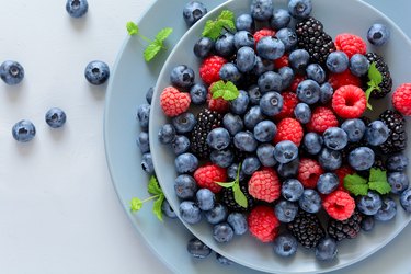 overhead photo of a blue bowl of blackberries, blueberries, raspberries and mint leaves on a gray background