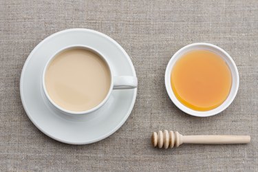 Spicy warming tea with milk in a white porcelain cup with honey and honey dipper