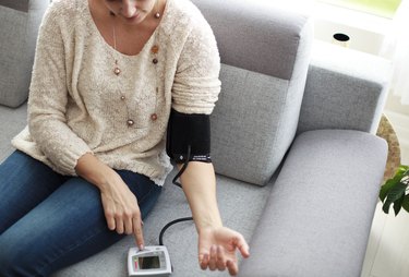 Person sitting on couch at home and measuring blood pressure to see the side effects of coffee