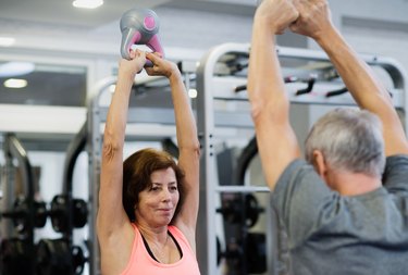 Senior couple in gym working out using kettlebells.