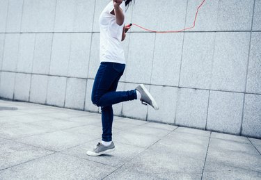Young fitness woman rope skipping against city wall