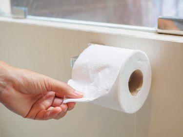 Closeup female hand picking a white tissue from tissue roll in the restroom.