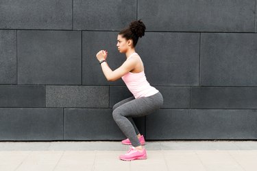 Side view of young athlete squatting at wall