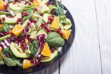 Leafy green salad with avocado, oranges and pomegranates on wooden table