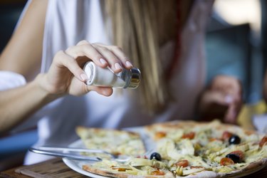 A woman salting pizza at a restaurant, as an example of what to avoid as a natural remedy for high blood pressure
