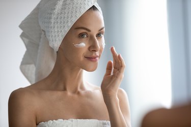 Close up beautiful woman applying cream, looking in mirror