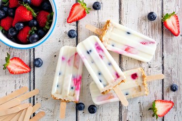 Mixed berry yogurt popsicles over a white wood background