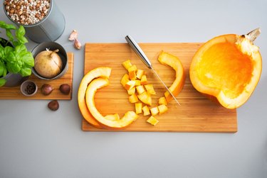 overhead photo of chopped raw pumpkin on a wooden cutting board