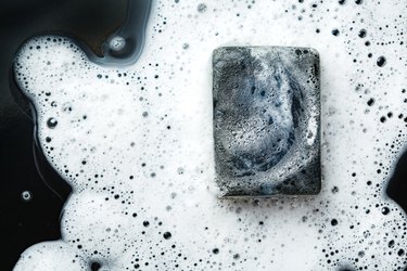 Black coal bar of soap in foam on dark