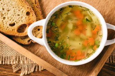 Chicken soup in white bowl on wooden tray.