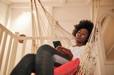 a person sitting in an indoor hammock using an anxiety app on their smartphone
