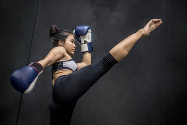 Young Asian woman boxer with blue boxing gloves kicking in the exercise gym