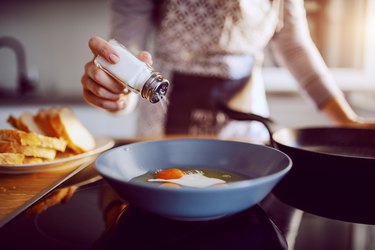 Close up of caucasian woman adding salt in sunny side up eggs seeking a low sodium treatment at home