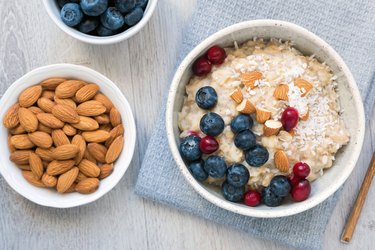 Oatmeal porridge with berry and nuts in white bowl. Table top view