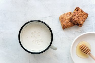 Hot milk in a cup and honey on a concrete table.