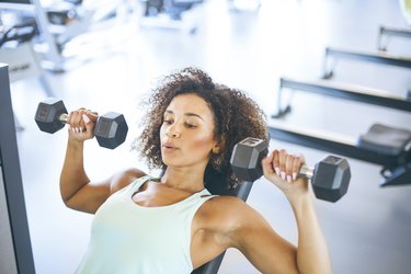 Person in a green tank top weightraining at the gym to lose weight