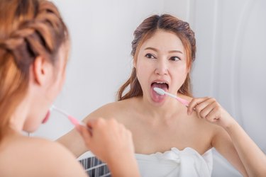 woman looking in bathroom mirror and brushing her tongue to get rid of white tongue