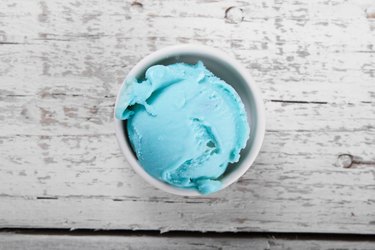 Scoop of tropical blue ice cream in bowl on white