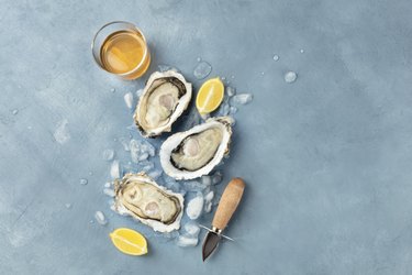 Fresh raw oysters, overhead shot on ice with a glass of white wine, lemon slices, shucking knife and a place for text