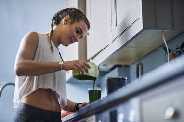Young woman pouring smoothie at kitchen counter