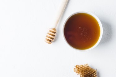 Fresh honey in a white cup on a white concrete background