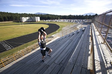 man in shorts running stairs with weighted vest and weight held above head