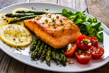 cooked salmon steak and asparagus on wooden table