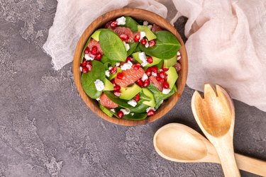 Tasty salad with grapefruit, spinach, feta, avocado and pomegranate in wooden bowl