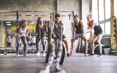 Group of young fit people cheering at man exercising with ropes in gym