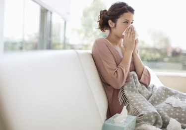 Sick woman blowing her nose on a couch