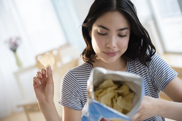 Hispanic woman reading ingredients on bag of potato chips