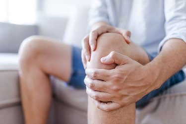 An older man sitting on the couch and massaging joint pain in his knee