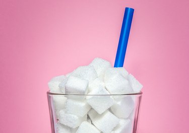 A close up of a glass full of sugar cubes with a blue straw on a pink background