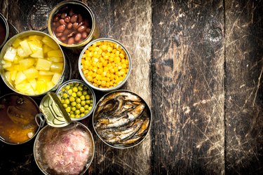 Various canned vegetables, meat, fish and fruits in tin cans.