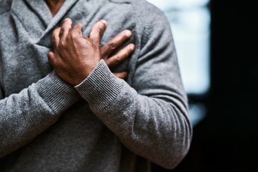 An older man holding his chest, suffering from a heart attack brought on by high blood pressure