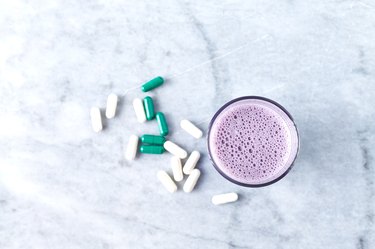 Glass of Protein Shake with milk and blueberries, Beta-alanine and L-Carnitine capsules in background. Sports bodybuilding nutrition. Stone background. Directly Above. Copy space.