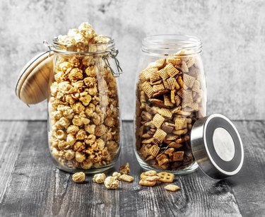 Two jars with caramelized popcorn and snack mix on gray background