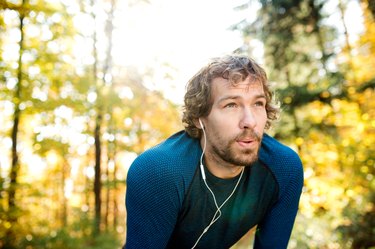 Young handsome runner with earphones outside in autumn nature