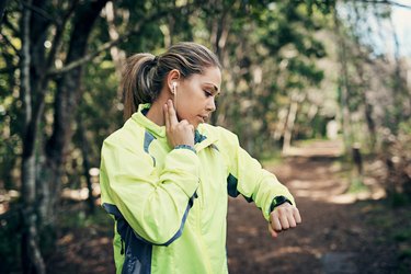 Person in a ponytail and neon yellow jacket checking their pulse while on a run outside.