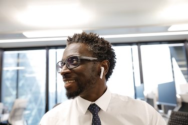 Businessman smiling, wearing earbud headphones, looking at laptop