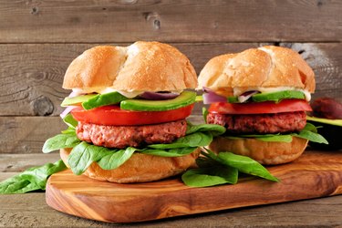 Plant based meatless burgers with avocado, tomato and spinach against a wood background