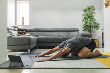 man doing a back stretch exercise on a gray yoga mat in his living room