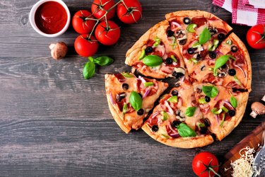 Homemade pizza with pepperoni, vegetables and basil, top view, corner border against a wood background with copy space