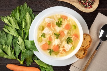 Chicken noodle soup close-up with ingredients on a dark rustic wooden background