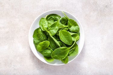 Fresh spinach. Green vegetable leaves on plate, healthy food, vegetarian diet concept.