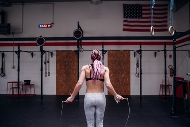 Young woman training, holding skipping rope in gym, rear view