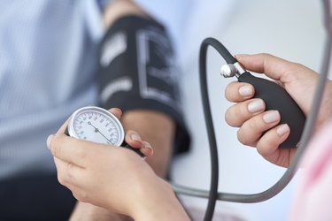 Close view of a nurse taking a patient's blood pressure to check it with a healthy blood pressure and high blood pressure range chart