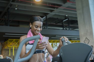 young latin woman trains in the gym elliptical while listening to music through her headphones