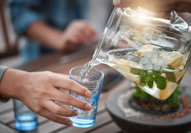 Close view of someone pouring a pitcher of water with lemons and mint into a glass