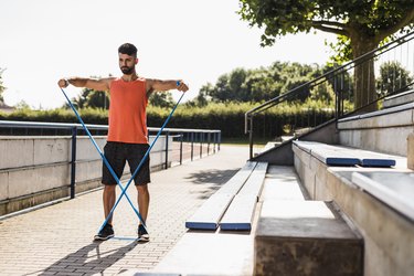 Man doing arm and ab exercises with a resistance band outside